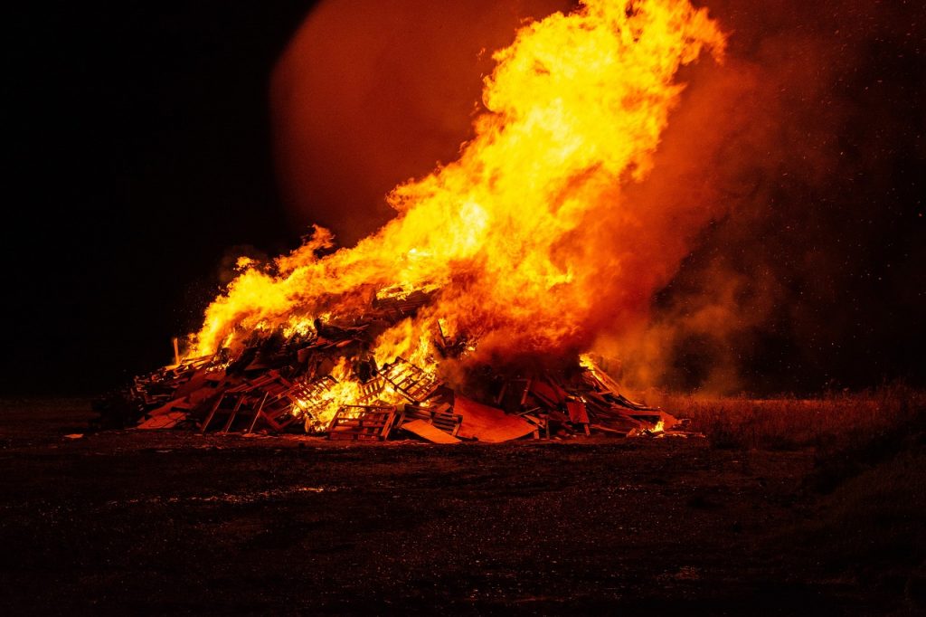 A flaming, towering pyre with wood, old furniture, and other flammable materials in it
